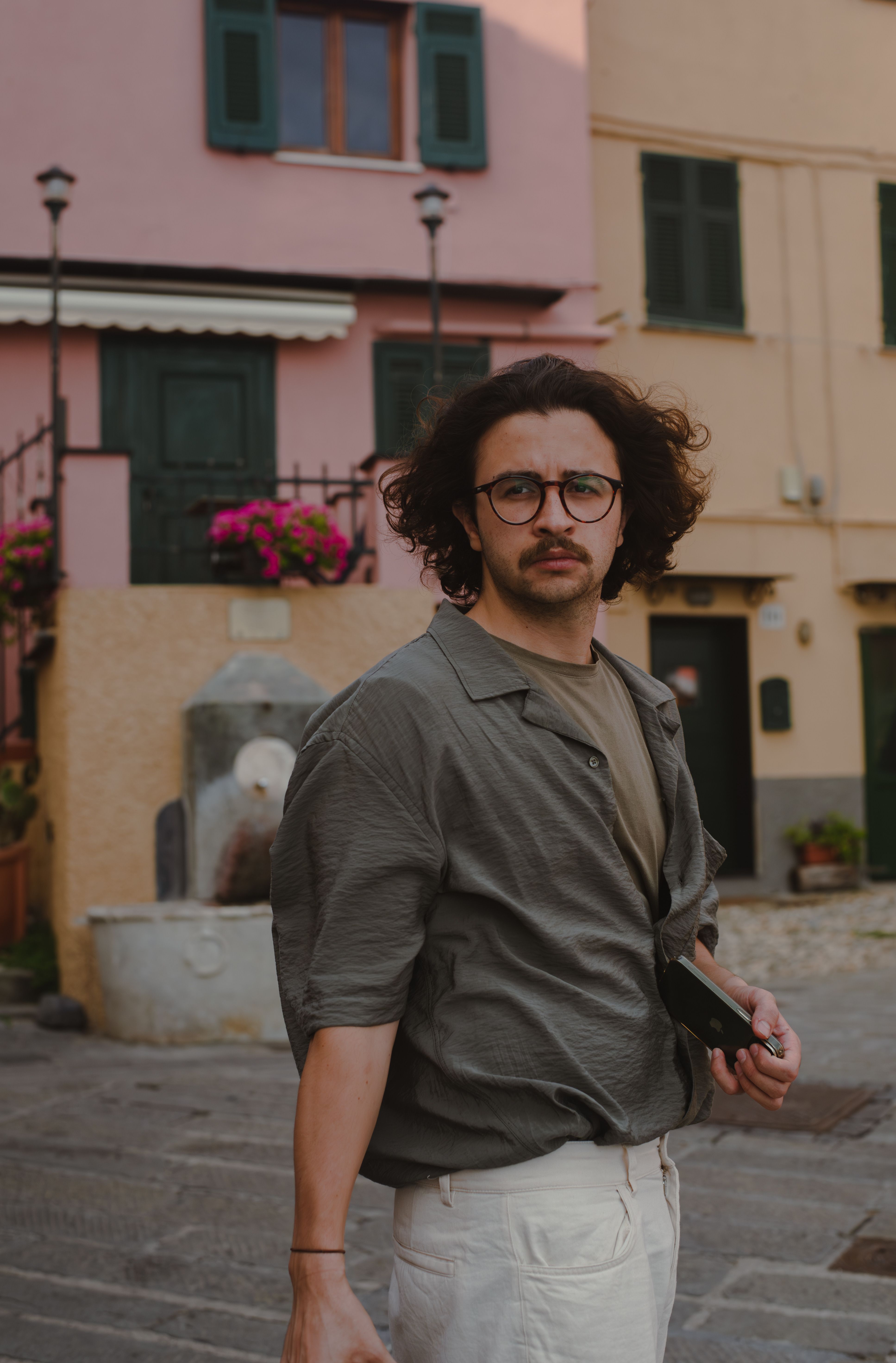 Fashionable man with eyeglasses posing outdoors in Genoa, Italy, near historic architecture.