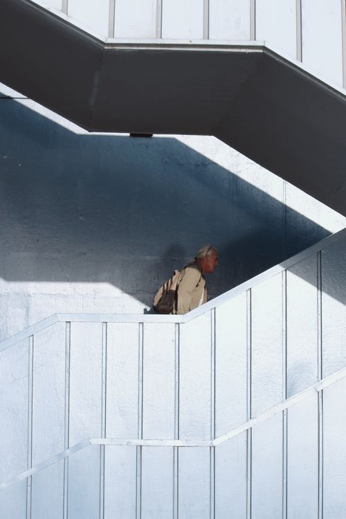 Free Man walking up a geometric, modern staircase in an urban setting, showcasing architectural lines. Stock Photo