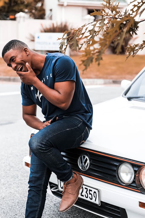 Hombre Vestido Con Camiseta Y Jeans Sentado En El Capó Del Coche Volkswagen Blanco