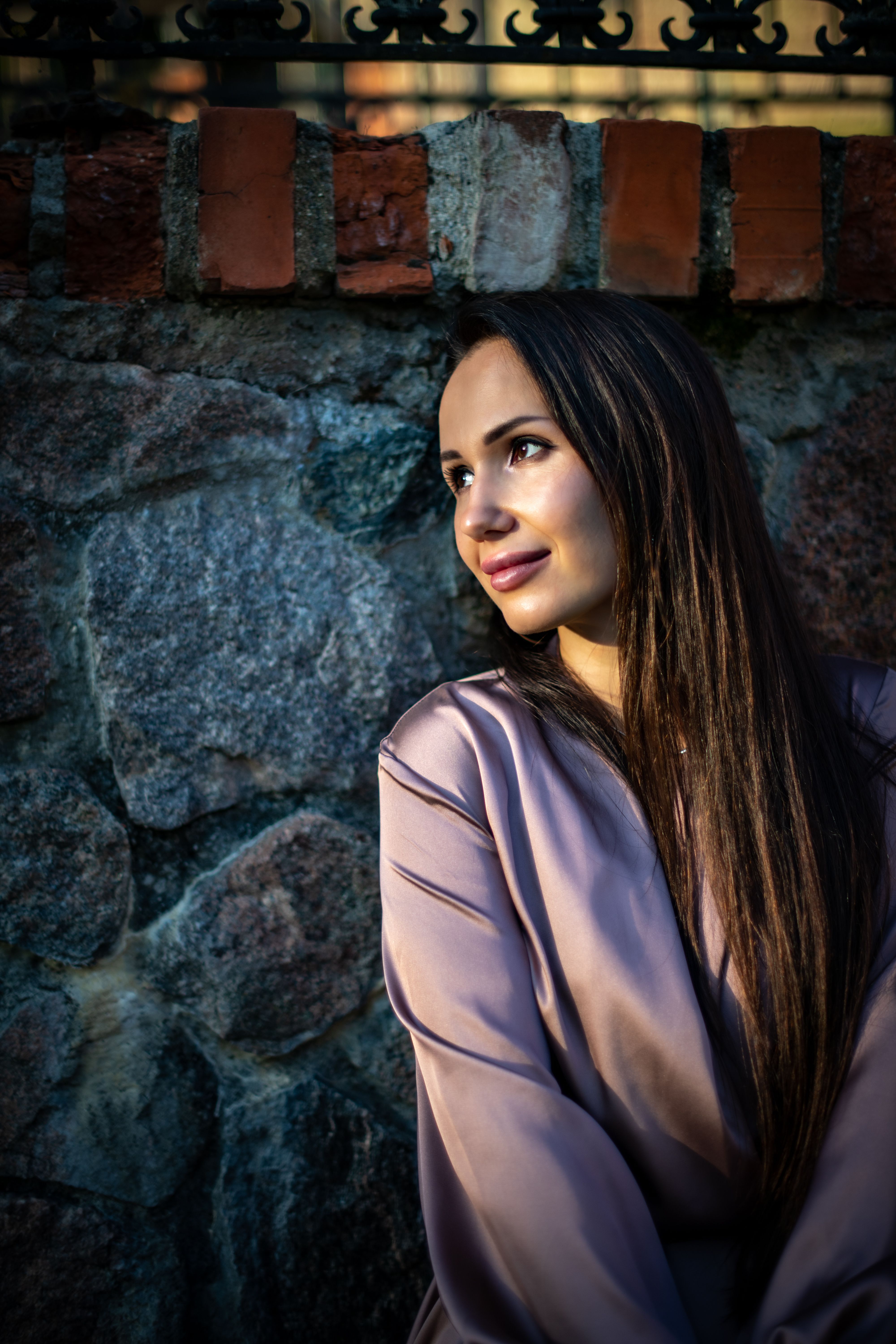 Charming portrait of a woman with long hair posing against a rustic stone wall in Vilnius.