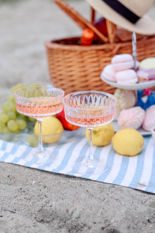 Free Relaxing beach picnic scene with drinks, fruits, and macarons on a striped blanket. Stock Photo