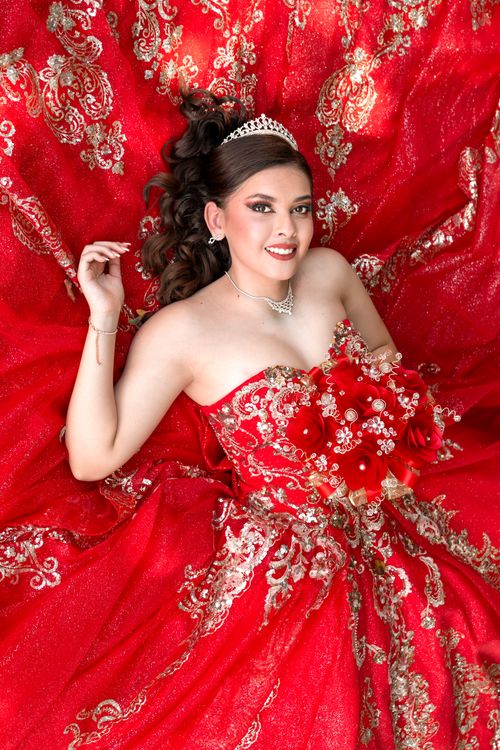 Free A beautiful woman in a red floral gown, smiling, holding a bouquet in a fashion pose. Stock Photo