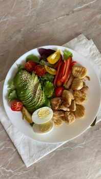 A vibrant salad of avocado, grilled chicken, and fresh vegetables on a ceramic plate.