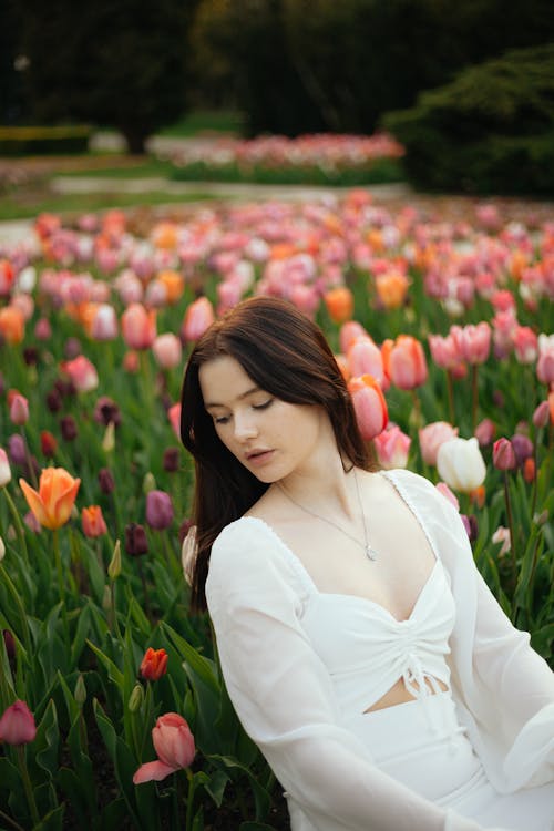 Woman in White Clothes Sitting among Tulips