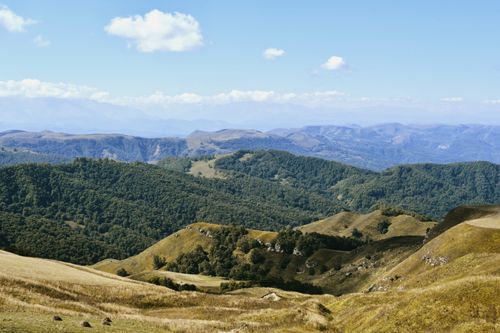 Free Expansive view of lush green hills and mountains under a clear blue sky. Stock Photo