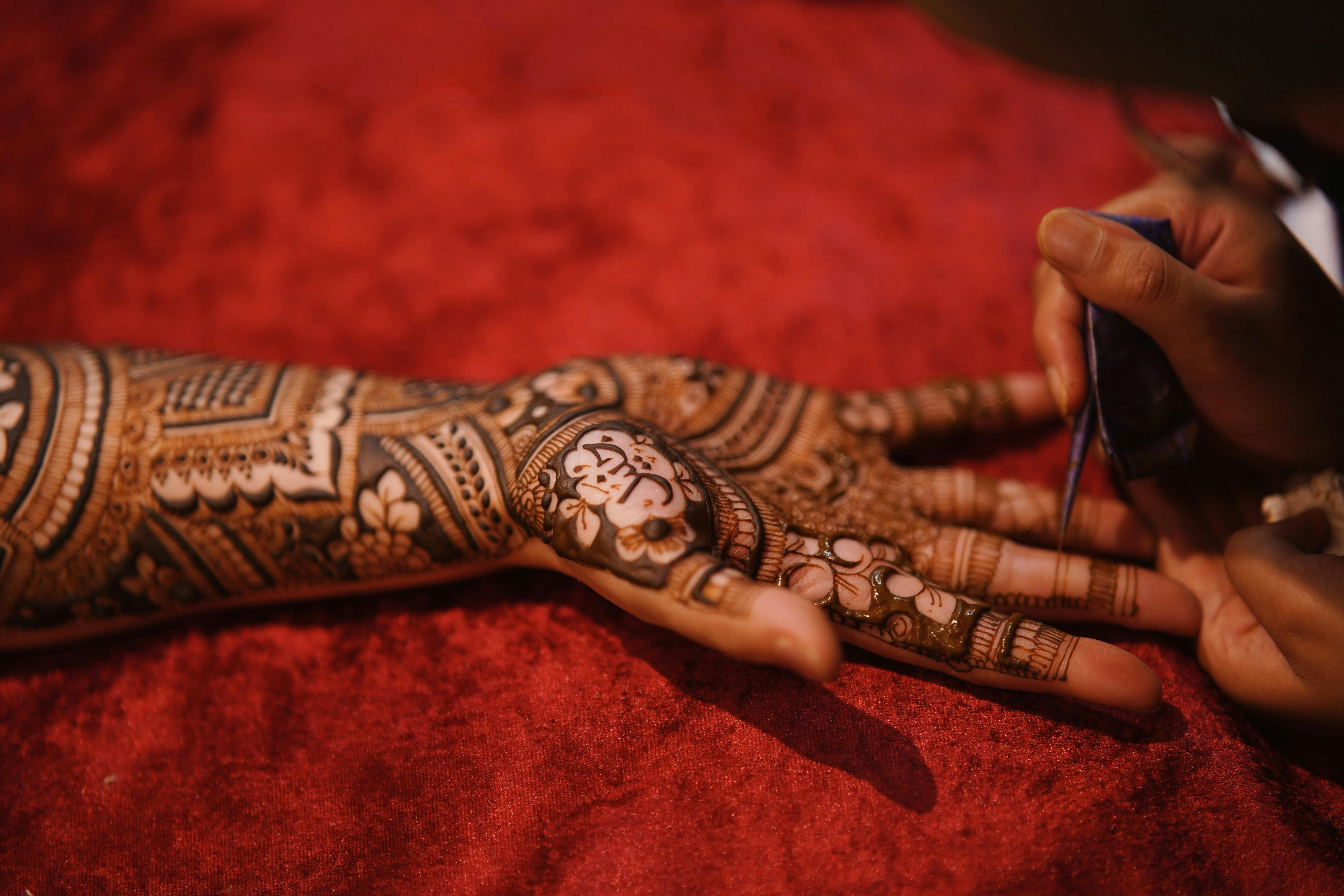 Close-up of a woman's hand being adorned with detailed henna tattoos showcasing traditional artistry.