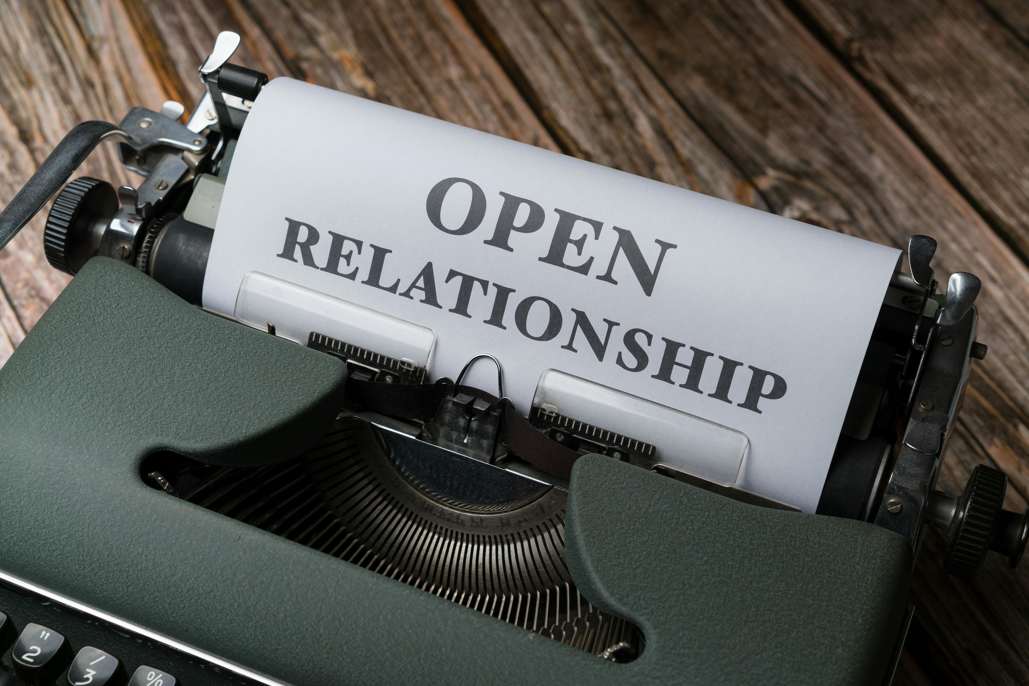A vintage typewriter displaying the typed words 'Open Relationship' over a wooden background.