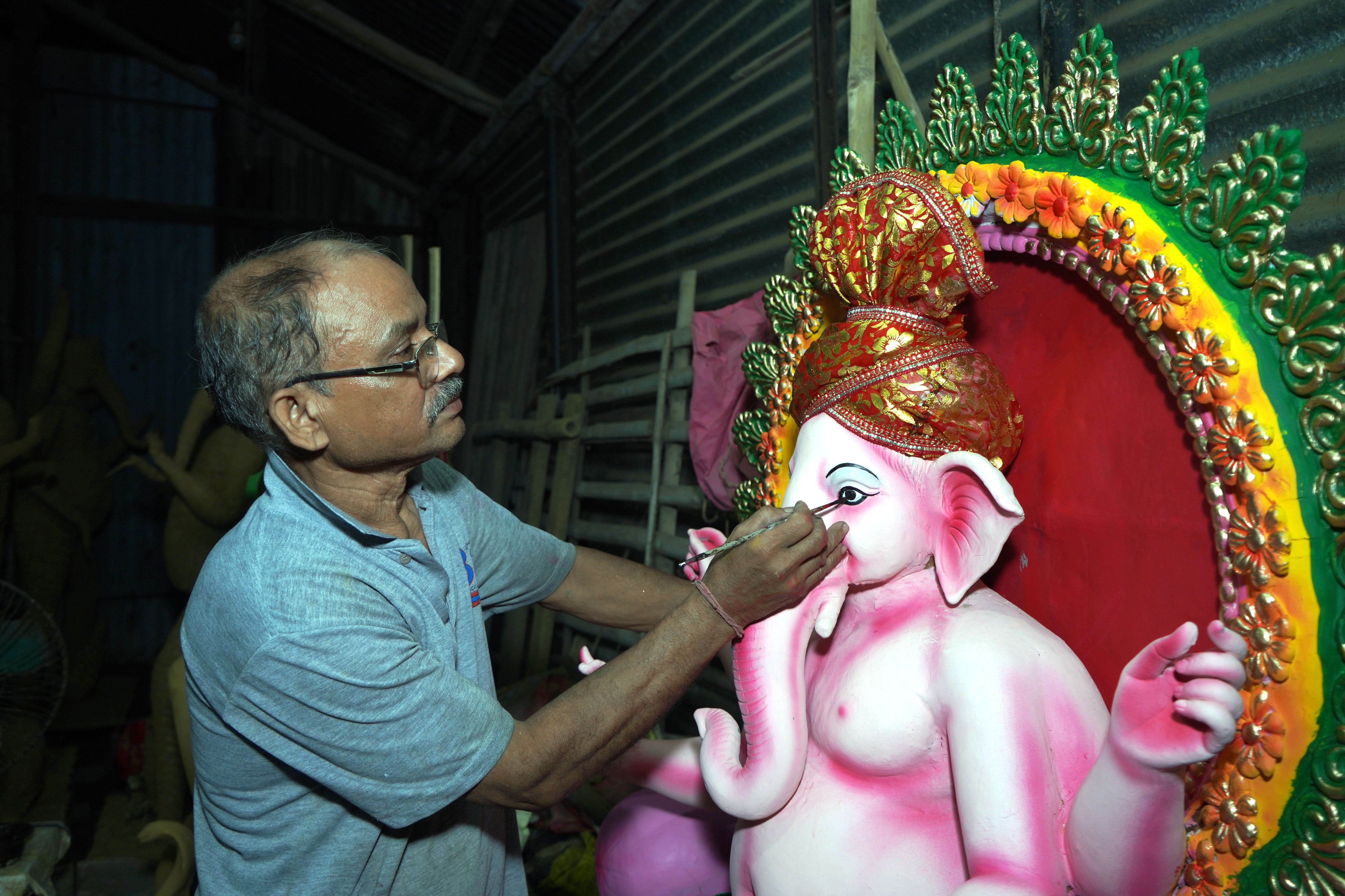 A skilled artist meticulously paints a vibrant Ganesha statue in an indoor workshop setting.