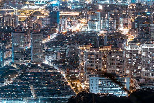 Aerial view of a bustling city illuminated by lights at night, showcasing skyscrapers and roads.