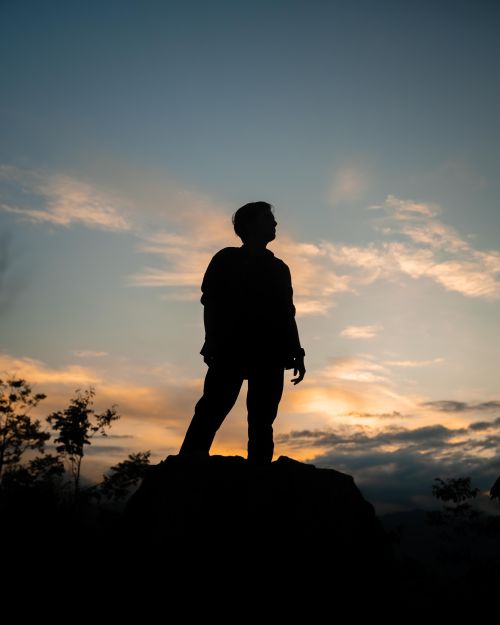 Free A dramatic silhouette of a man standing on a rock against a sunset sky in San Martín, Peru. Stock Photo