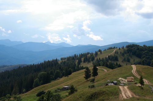 Free Scenic view of rolling hills and mountains with a winding dirt road under a cloudy sky. Stock Photo