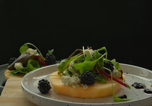 Appetizing salad with blackberries, blue cheese, and greens on a white plate with dark background.
