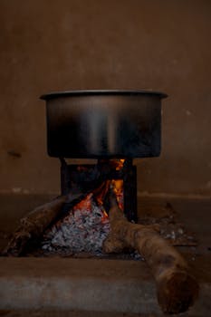 A metal pot on a stove with firewood and open flame, perfect for traditional cooking.