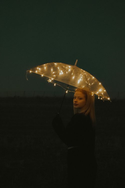 Free A woman holding a glowing umbrella stands amidst darkness, creating a magical night scene. Stock Photo