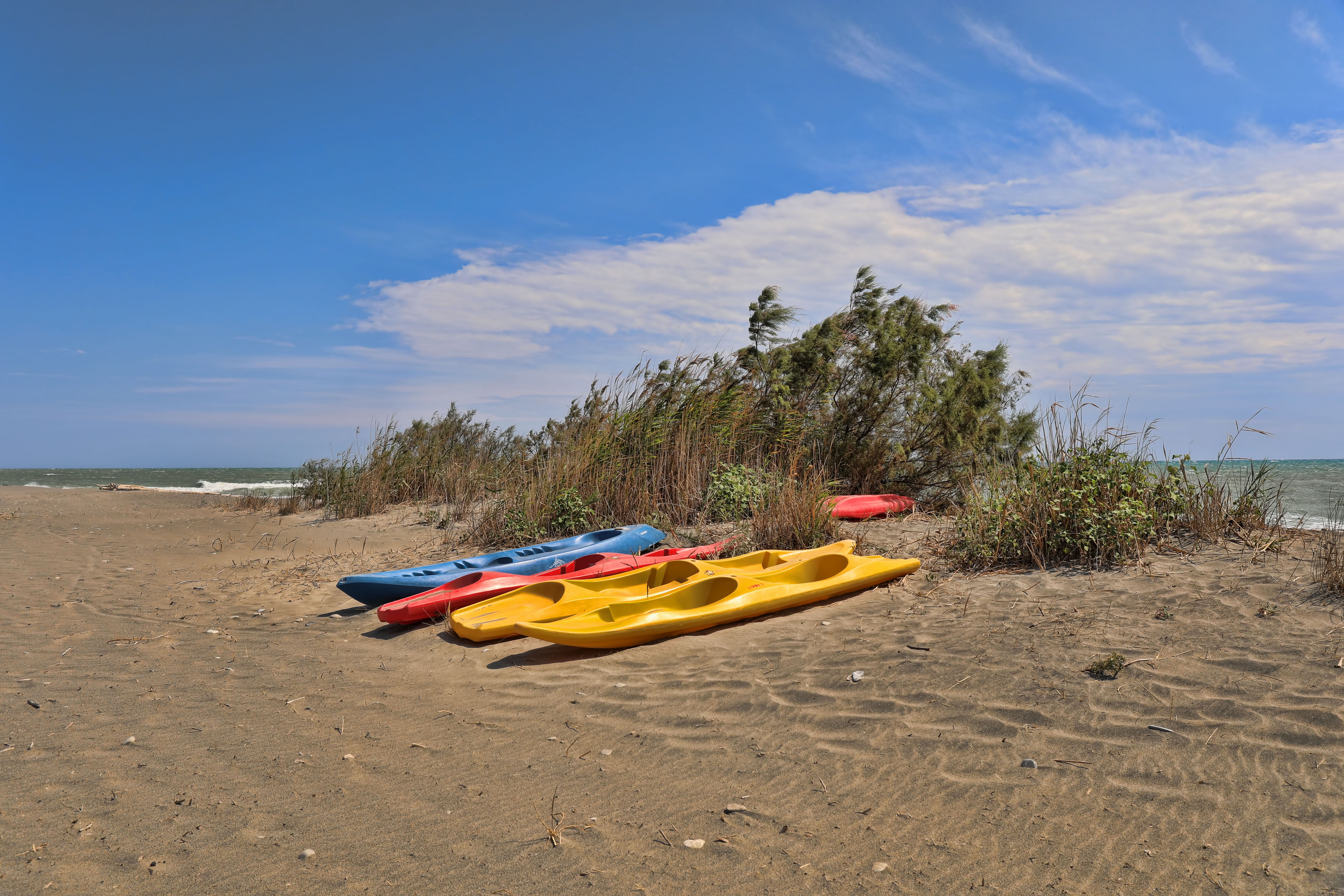 Vibrant kayaks on the sandy shoreline of Lido di Policoro under a clear sky.