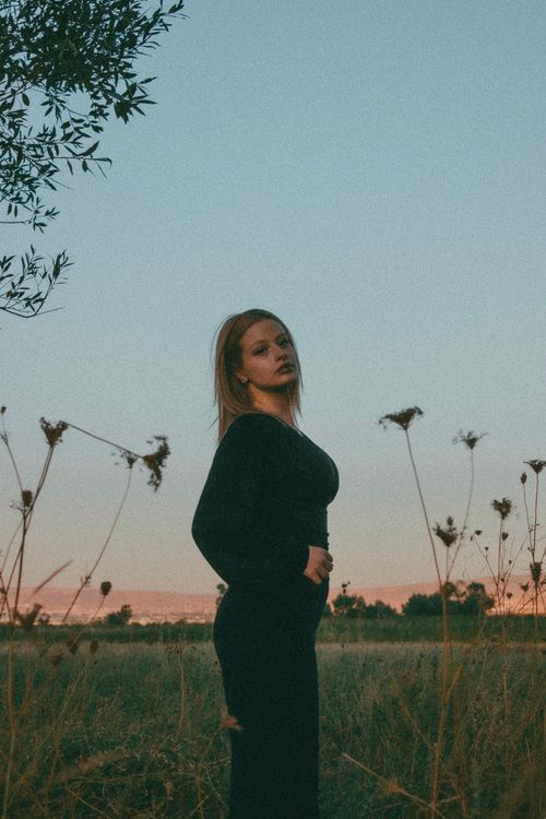 Free A woman dressed in black poses in a rural grassland setting in Ankara, Türkiye during sunset. Stock Photo