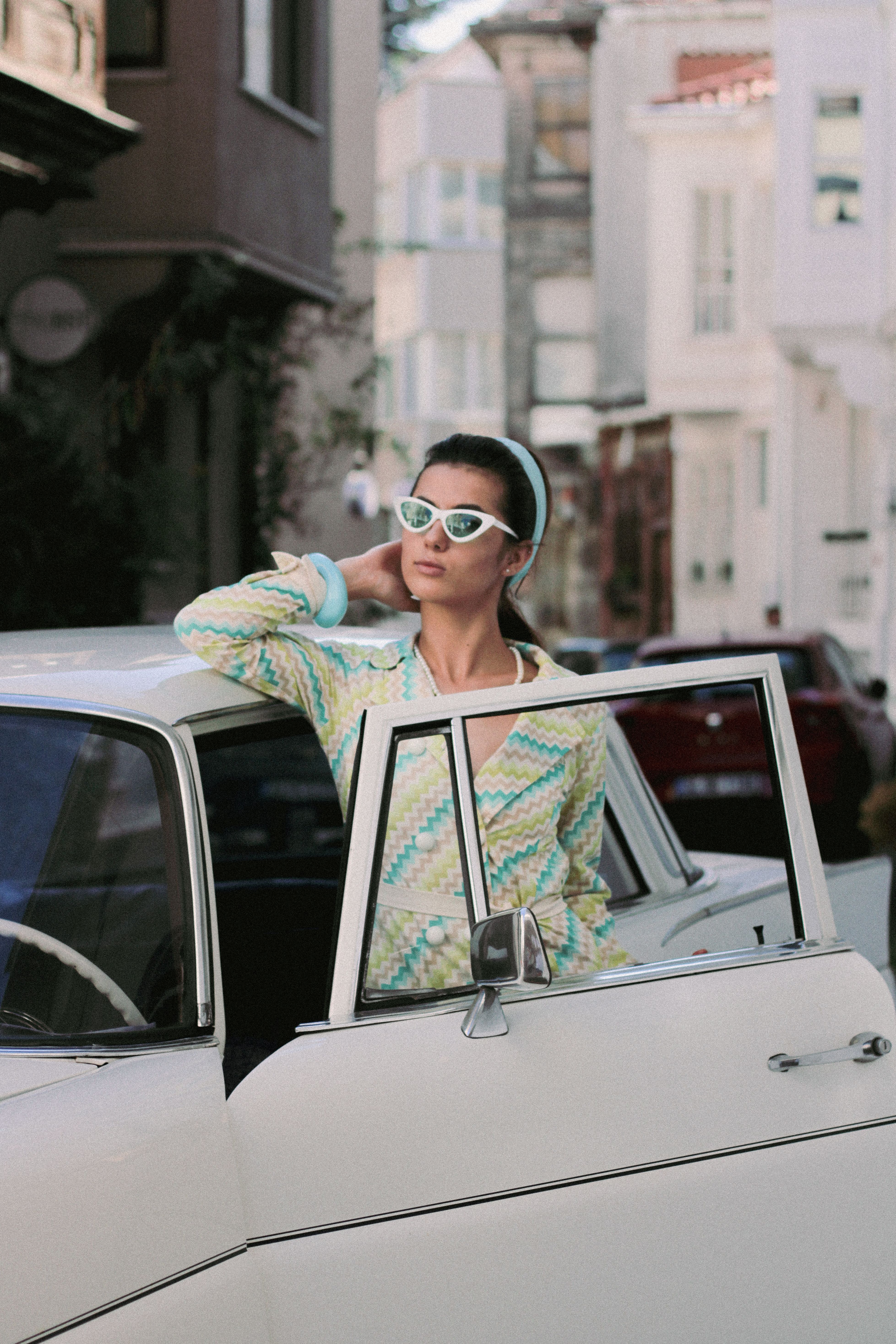 Fotomural Mujer elegante con atuendo retro posando con un coche vintage en una calle de la ciudad.