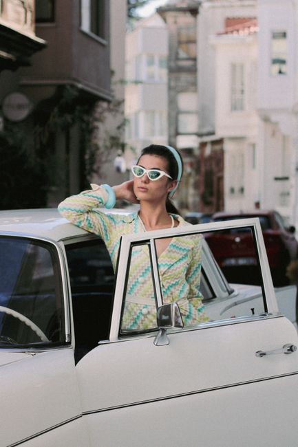 Fotomural Mujer elegante con atuendo retro posando con un coche vintage en una calle de la ciudad.
