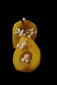 A vibrant yellow pear in a close-up shot against a black background, topped with crumbles.