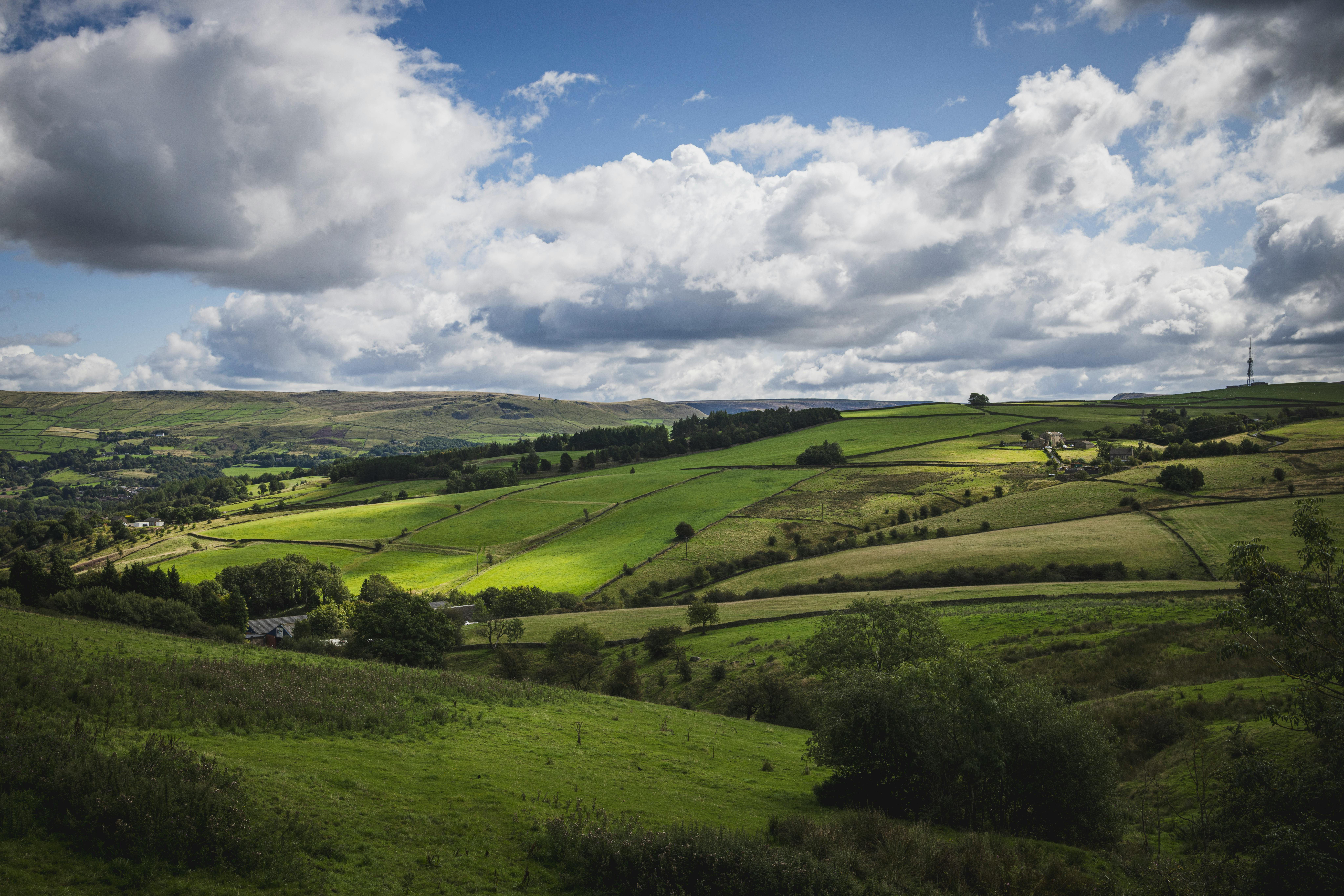 Beautiful lush green landscape featuring rolling hills and farmlands under a bright sky in Oldham, England.
