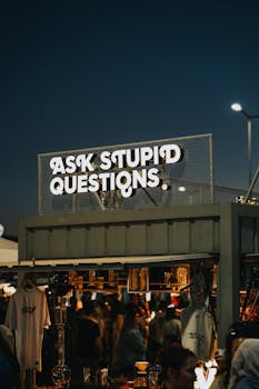 Colorful night market stall in Ankara featuring illuminated sign 'Ask Stupid Questions'.