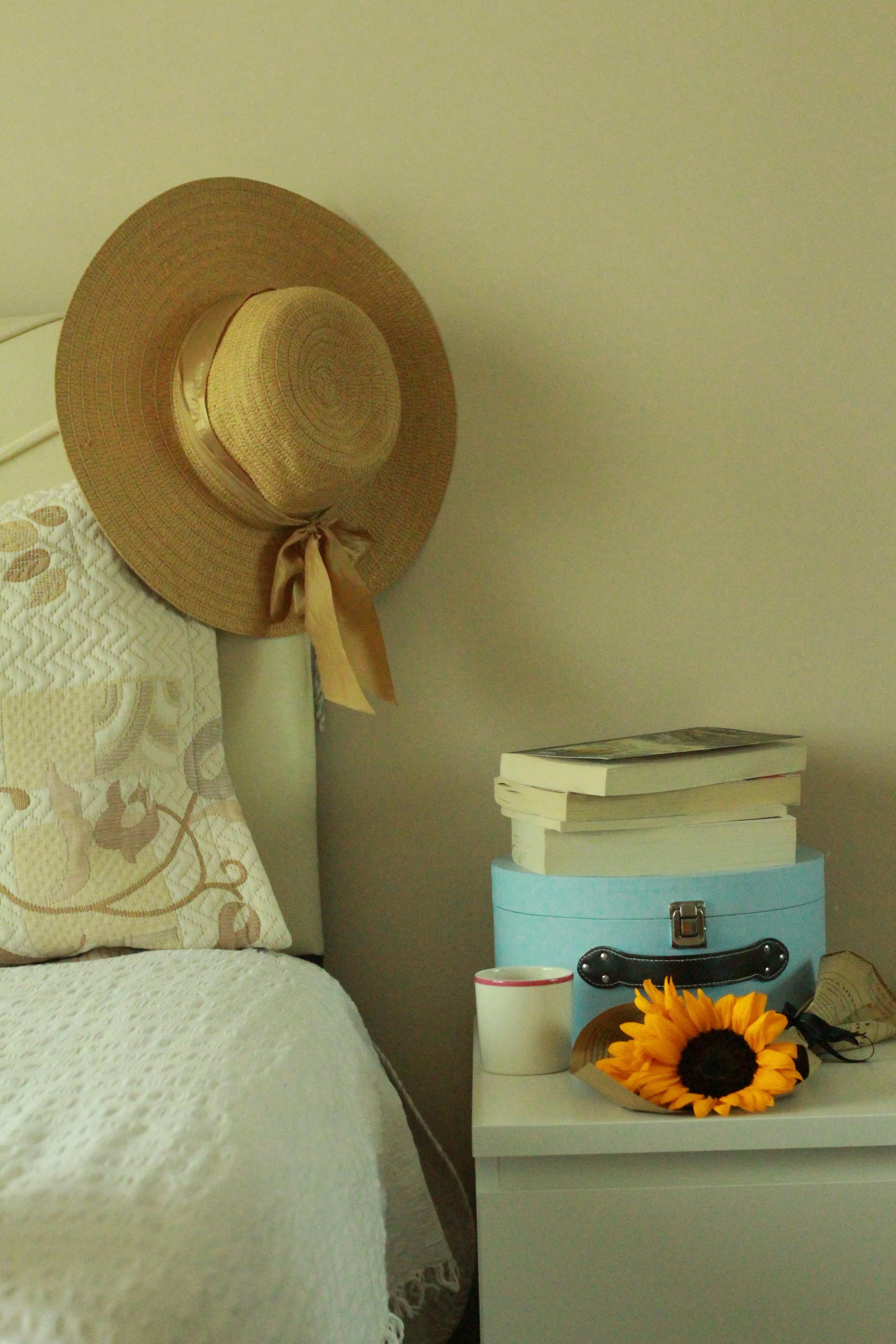 A cozy bedroom scene featuring sunflowers, a straw hat, and stacked books.