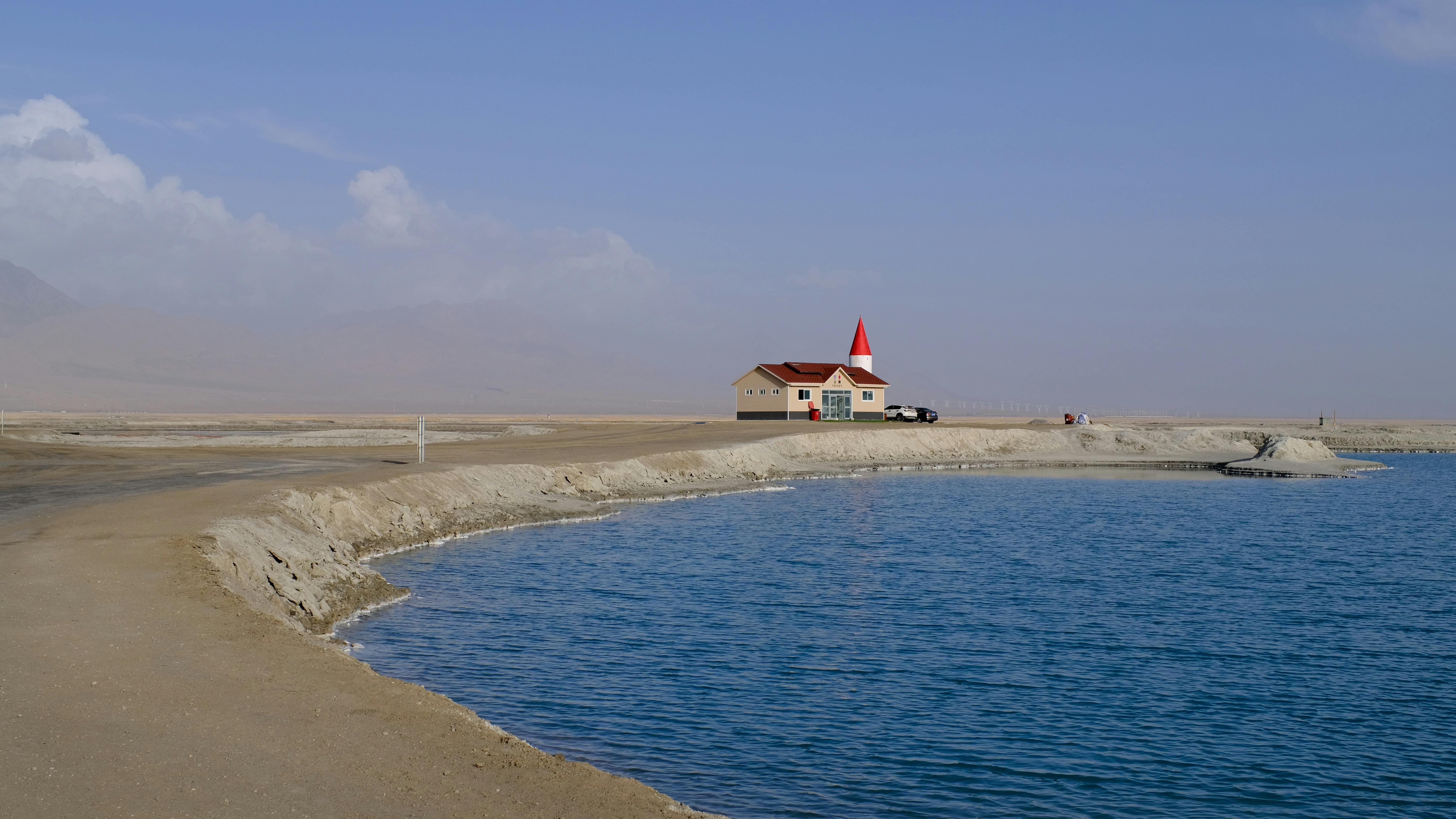 A serene lakeside scene featuring a building with a red roof and tower against a clear blue sky.