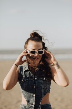 Stylish young woman with sunglasses on a breezy beach enjoying a sunny day.