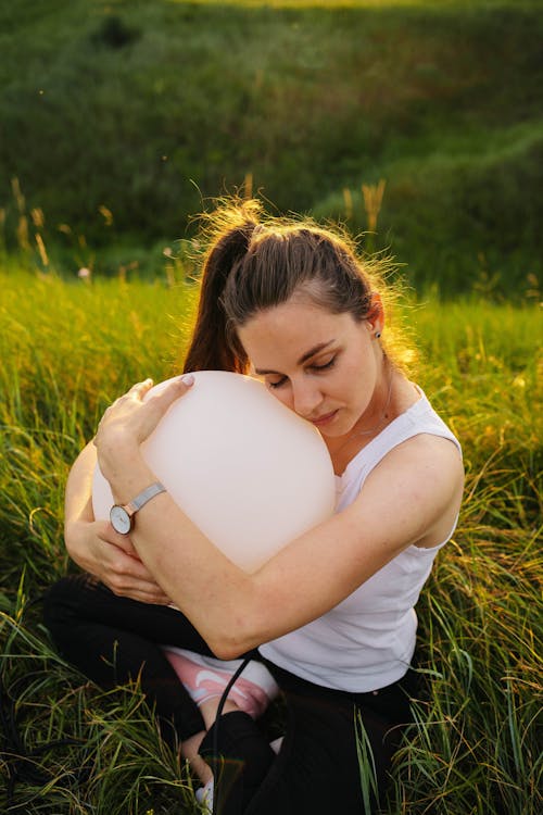 A Woman Sitting on a Meadow and Hugging a Balloon 