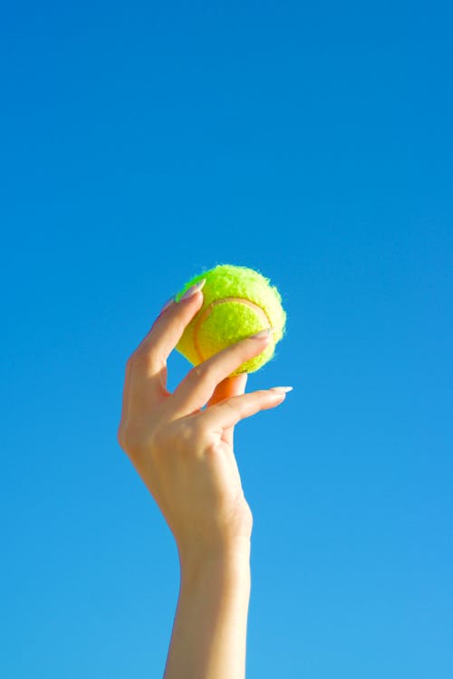 Close-up of a Person Holding a Tennis Ball on the Background of Blue Sky