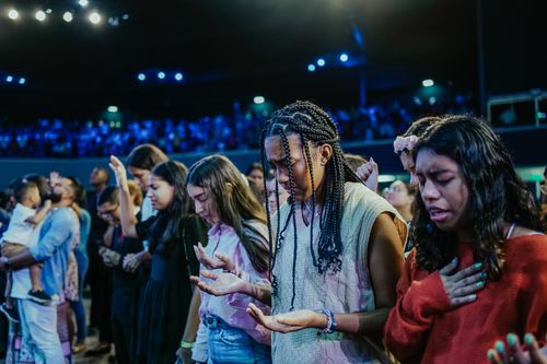 Free A heartfelt scene of young people gathered in prayer during a large indoor event. Stock Photo