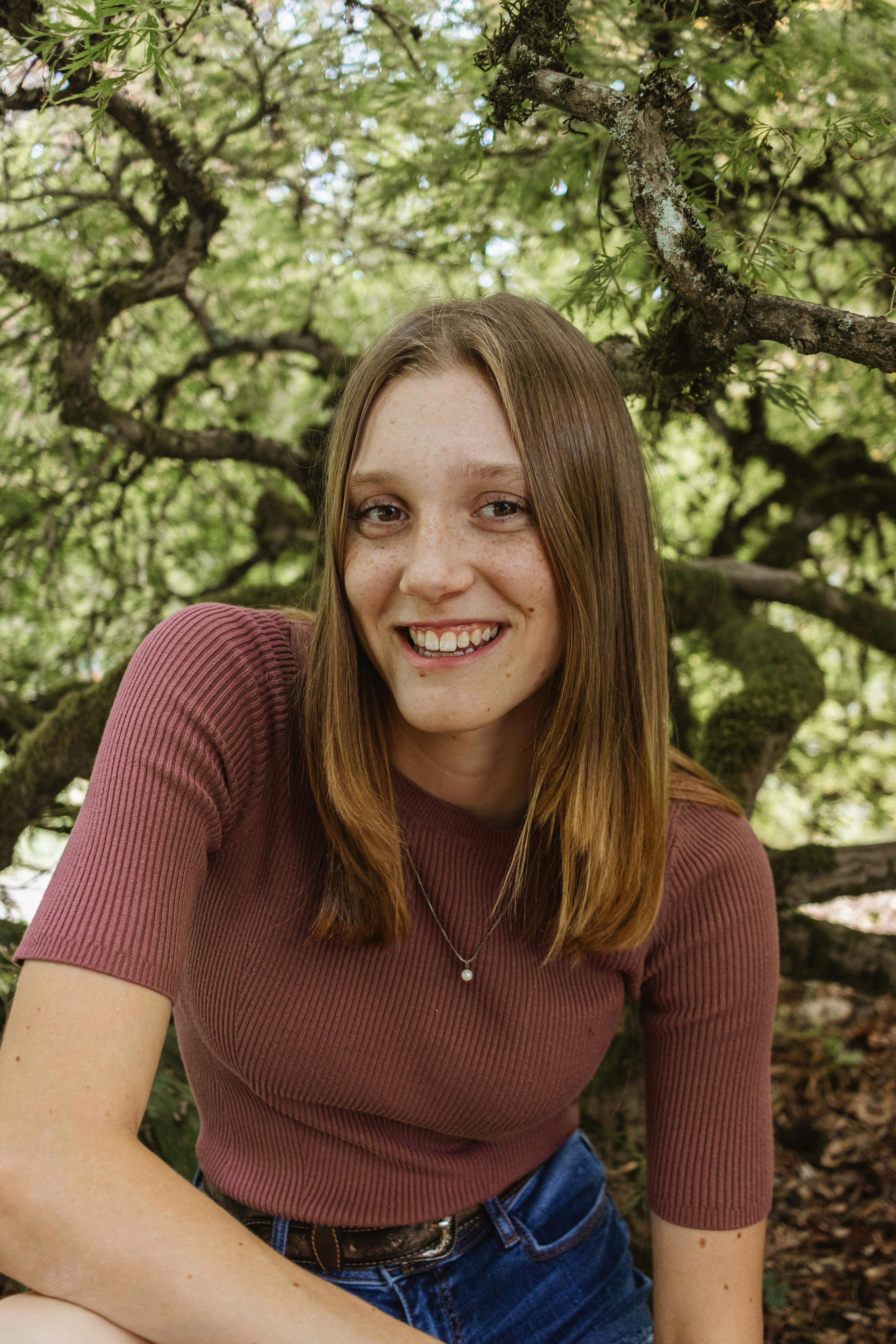 Portrait of a smiling woman with long brown hair amidst lush greenery.