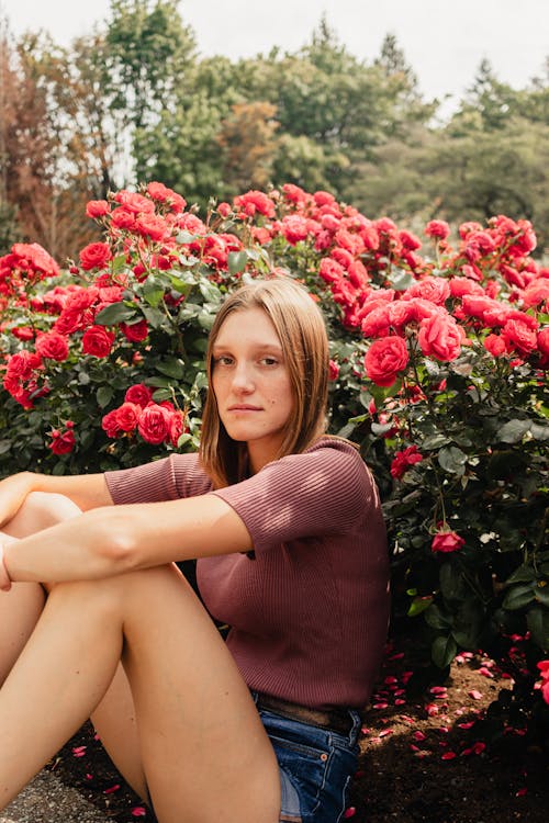 Young Woman Sitting between Roses in the Garden 