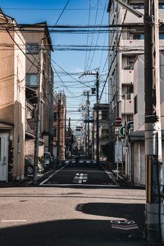 A quiet, narrow urban street with buildings and power lines on a sunny day.