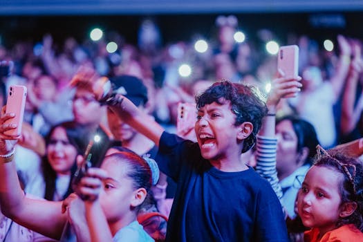Energetic kids enjoy a vibrant music concert, capturing moments on smartphones.