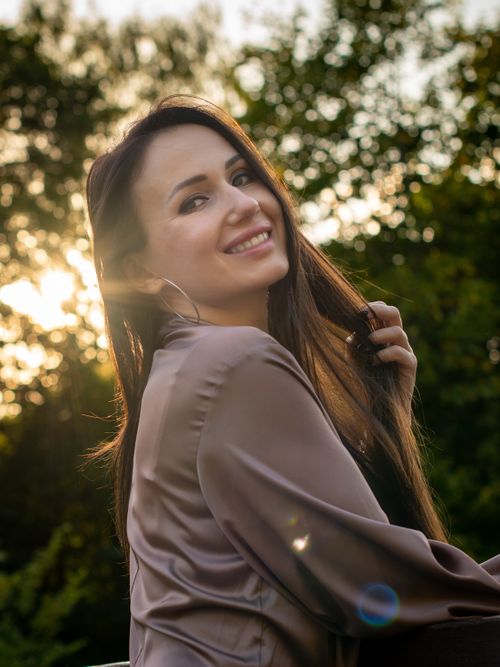 Free Portrait of a woman with long hair smiling outdoors in Vilnius park during sunset. Stock Photo
