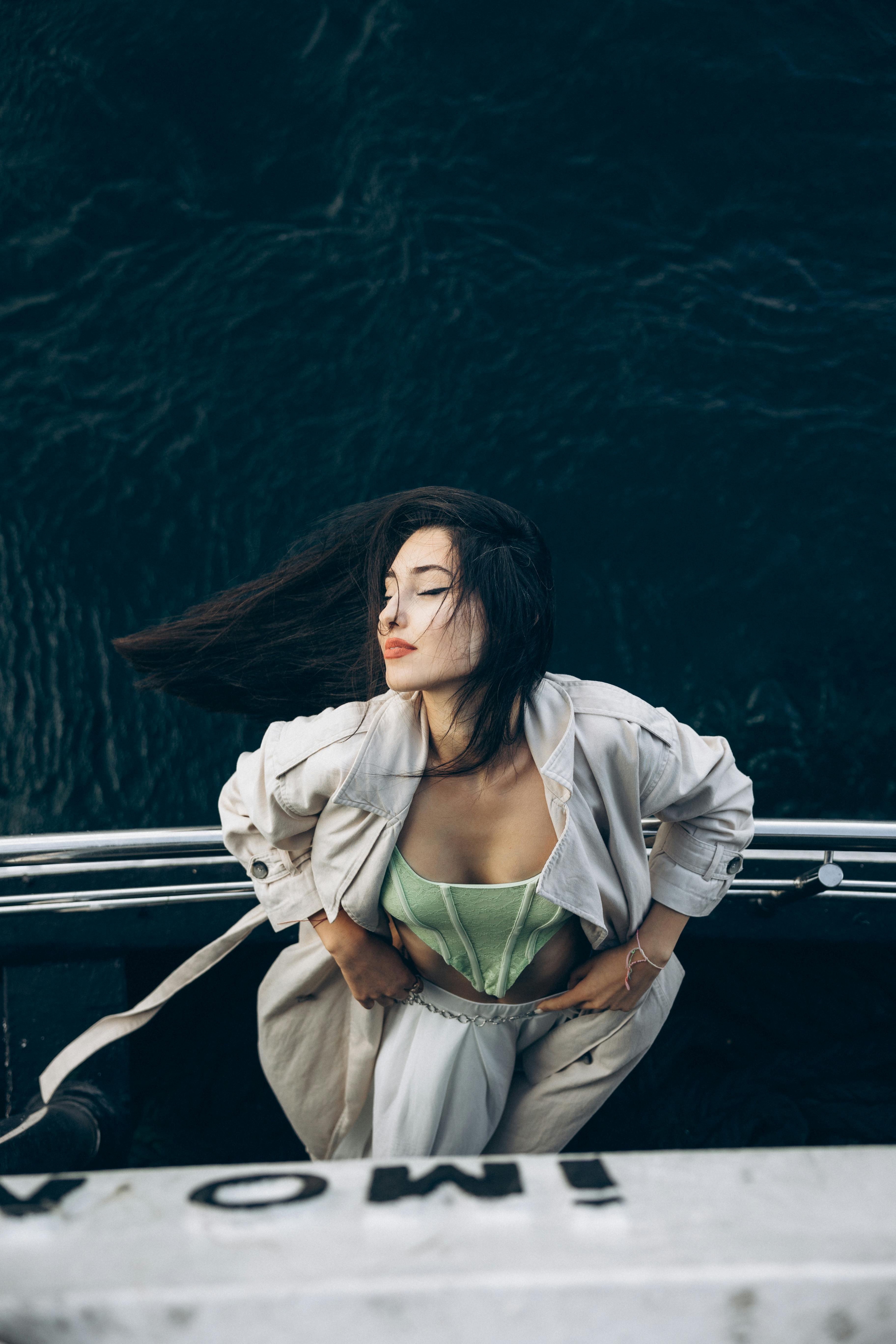 a woman in a green top and white pants is standing on the side of a boat