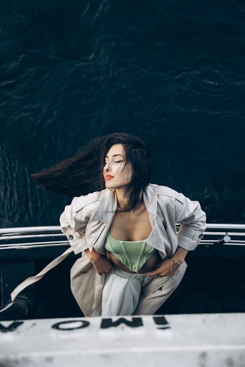 A woman in a green top and white pants is standing on the side of a boat