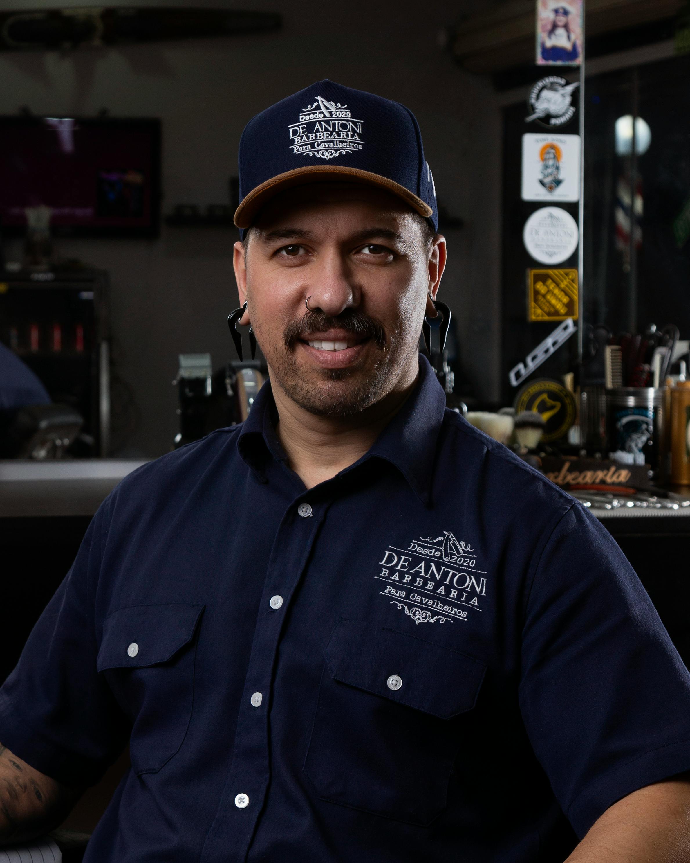 Smiling man in barber uniform at a trendy barbershop, exuding style.