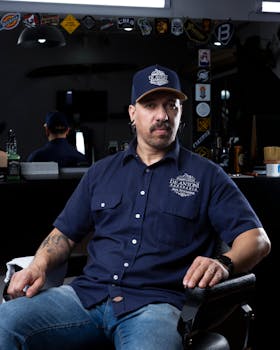 A modern barber seated in a stylish salon, wearing casual attire, reflects dedication to craft.