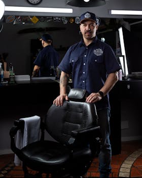Portrait of a barber standing confidently in a modern barbershop with dark decor and stylish ambiance.