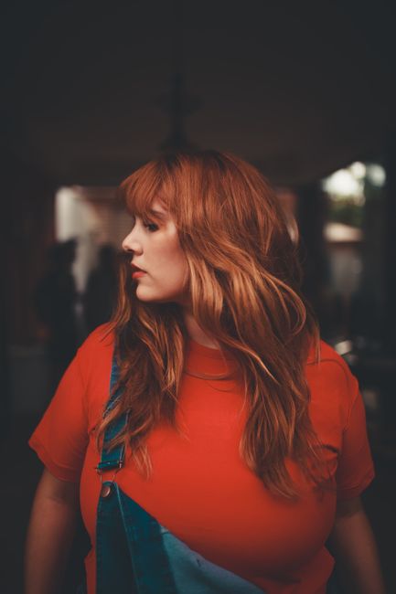 A captivating side profile portrait of a woman with red hair in a vibrant setting, showcasing modern fashion.