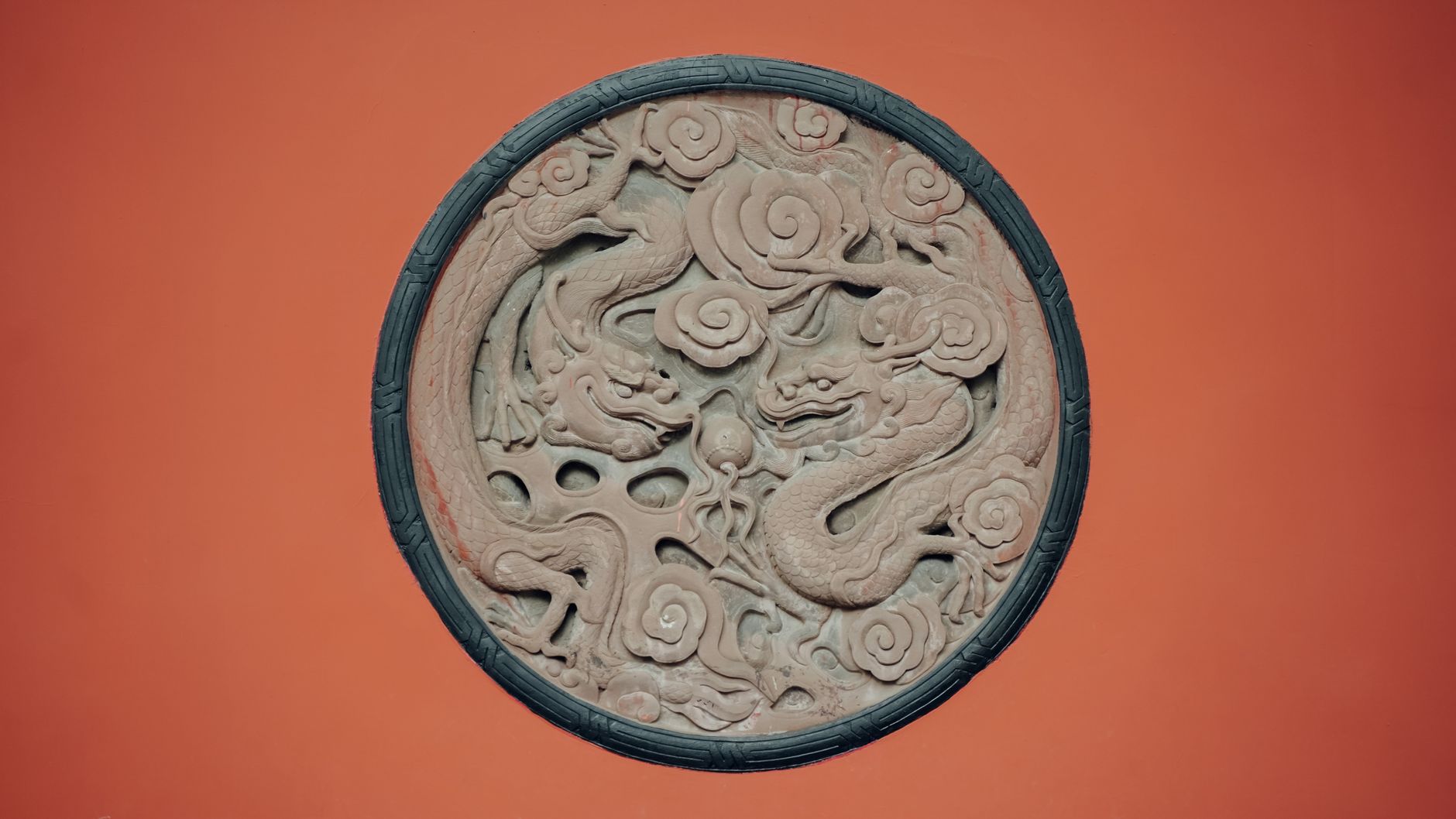 Beautiful ancient Chinese dragon bas-relief on red background featuring intricate carvings and cloud motifs.
