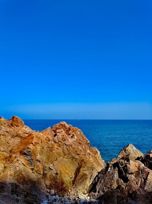 Free A serene coastal view with rugged rocks against a pristine blue sky and calm sea. Stock Photo