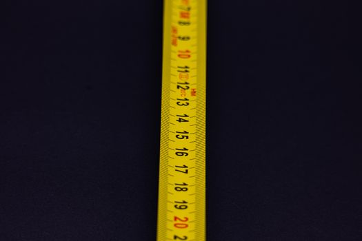 Detailed shot of a yellow measuring tape with numbers on a dark background.