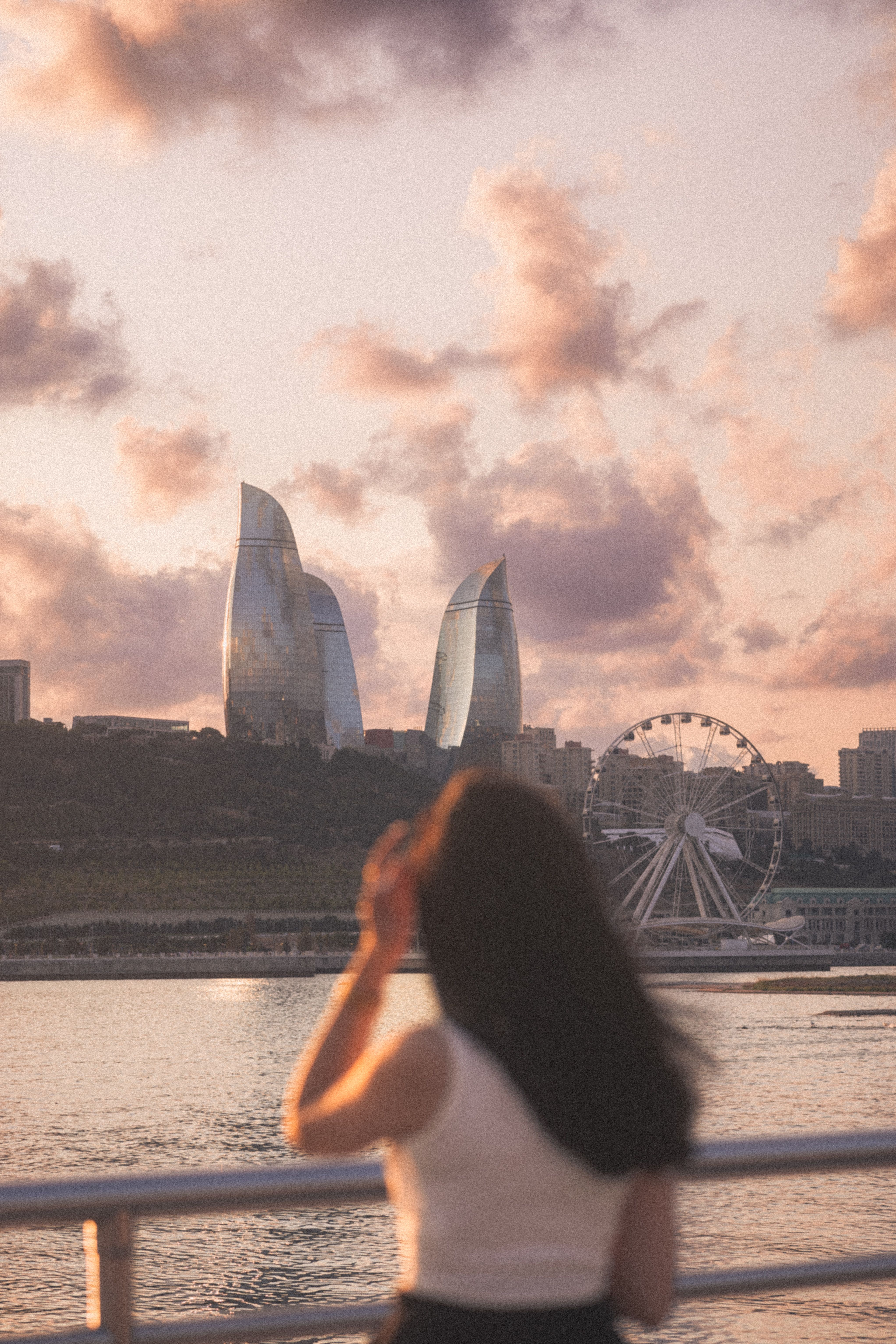 Silhouette of a woman gazing at Baku's iconic Flame Towers and Ferris wheel during a stunning sunset.