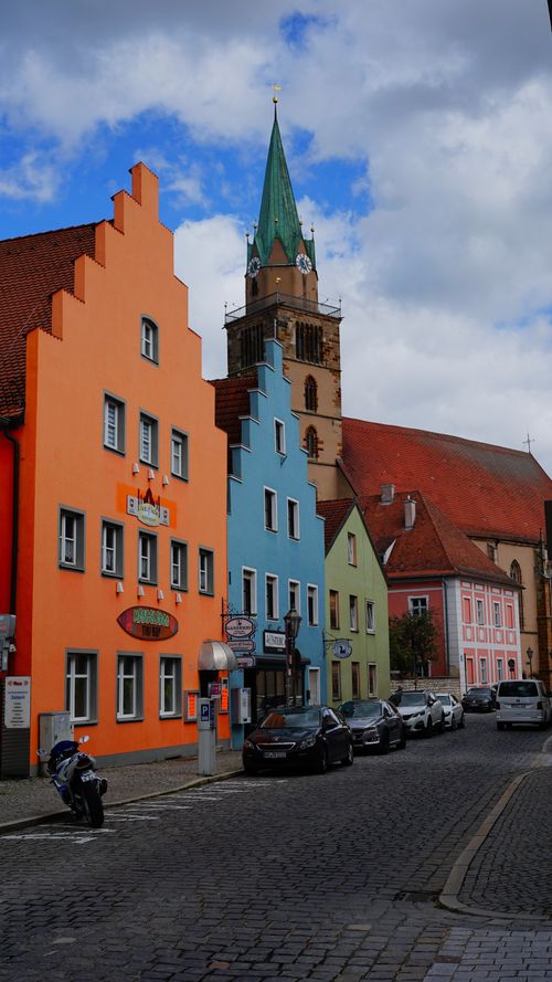 Free Vibrant street view of a European town with colorful buildings and a historic church tower under a cloudy sky. Stock Photo