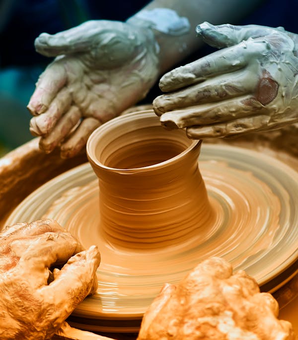 Hands shaping clay on pottery wheel