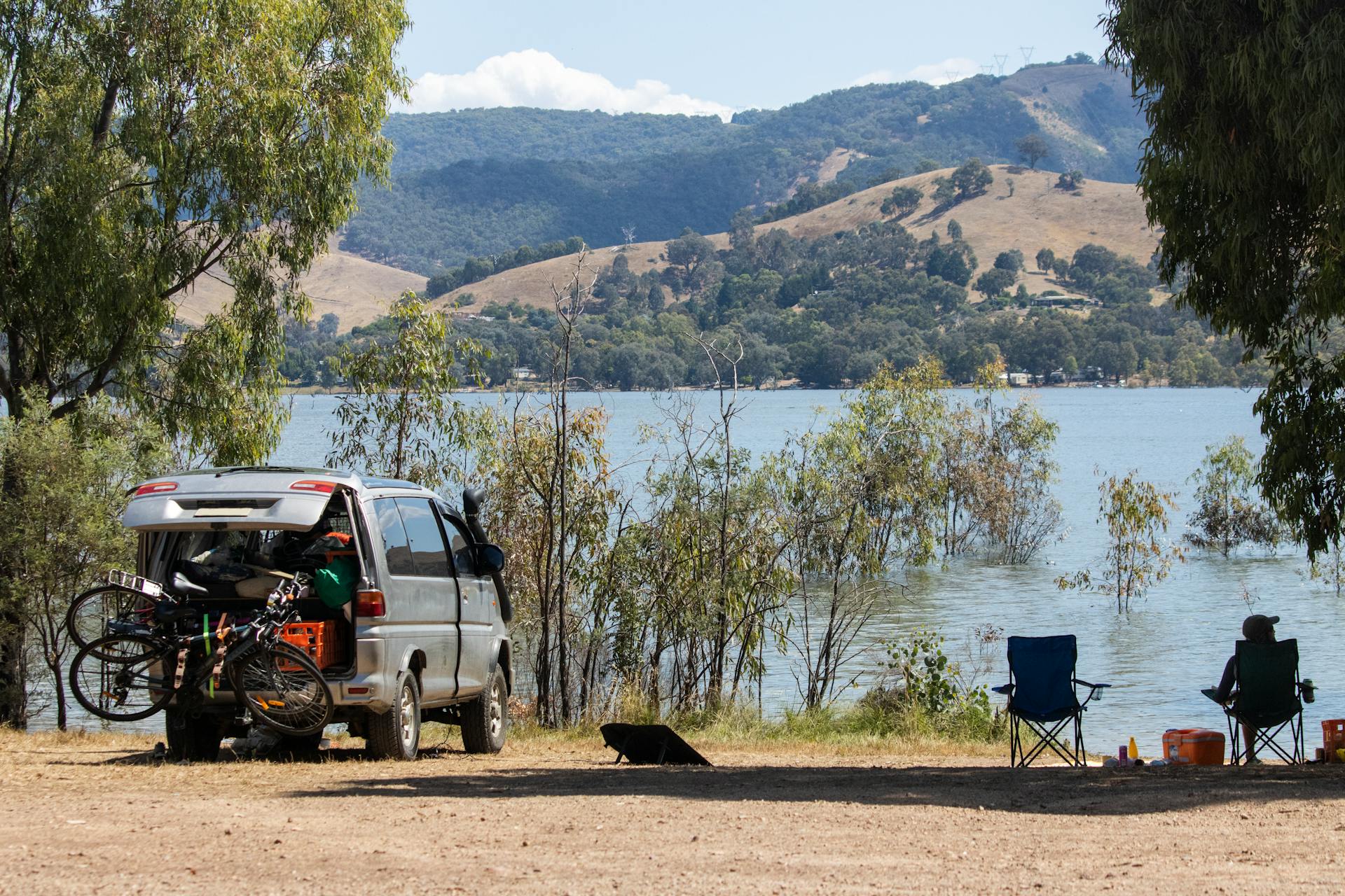 Relaxing camping scene by Lake Eildon with van, bikes, and chairs in Bonnie Doon, Australia.