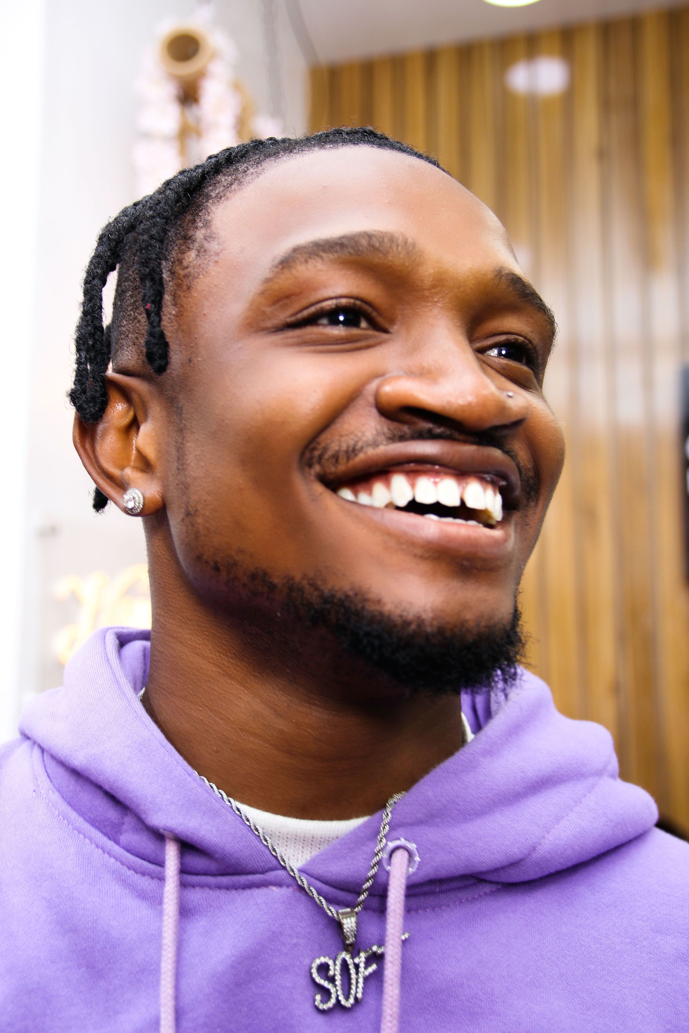 Portrait of a smiling man wearing a purple hoodie and jewelry in an indoor setting.